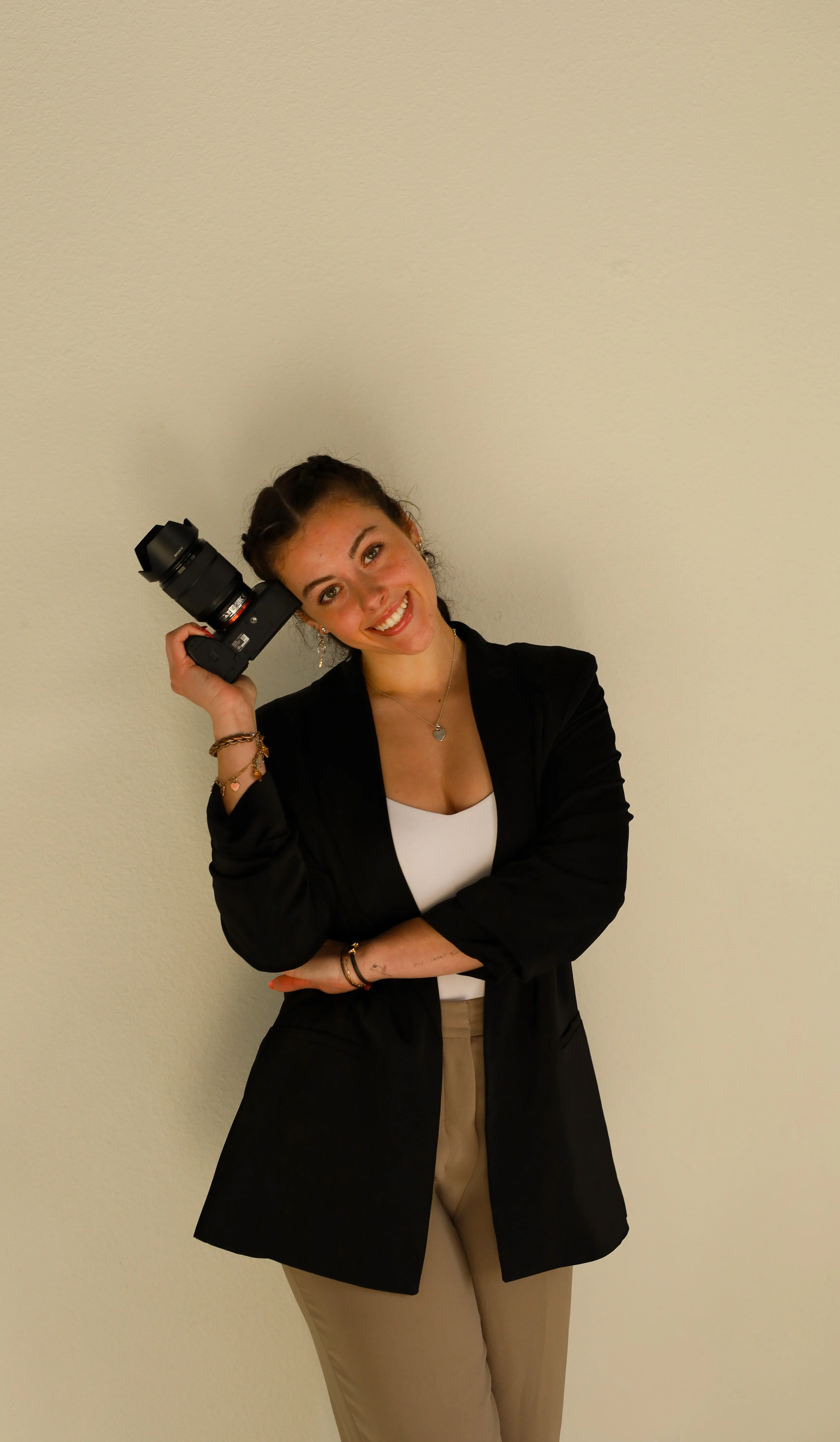 Baylie Mason holding a camera in a black blazer against a studio backdrop