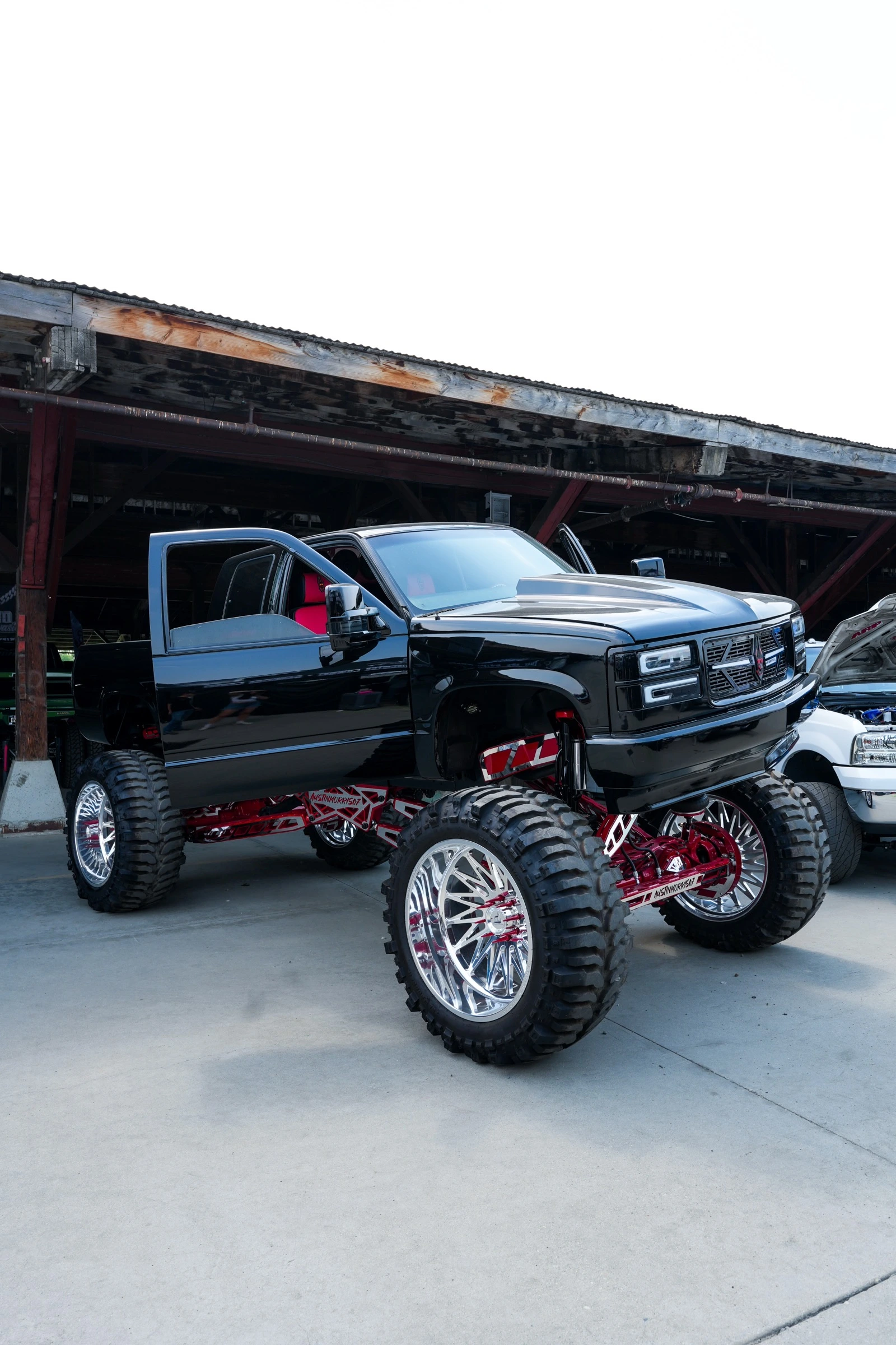 Glossy black lifted pickup truck with red suspension parked by a wooden barn