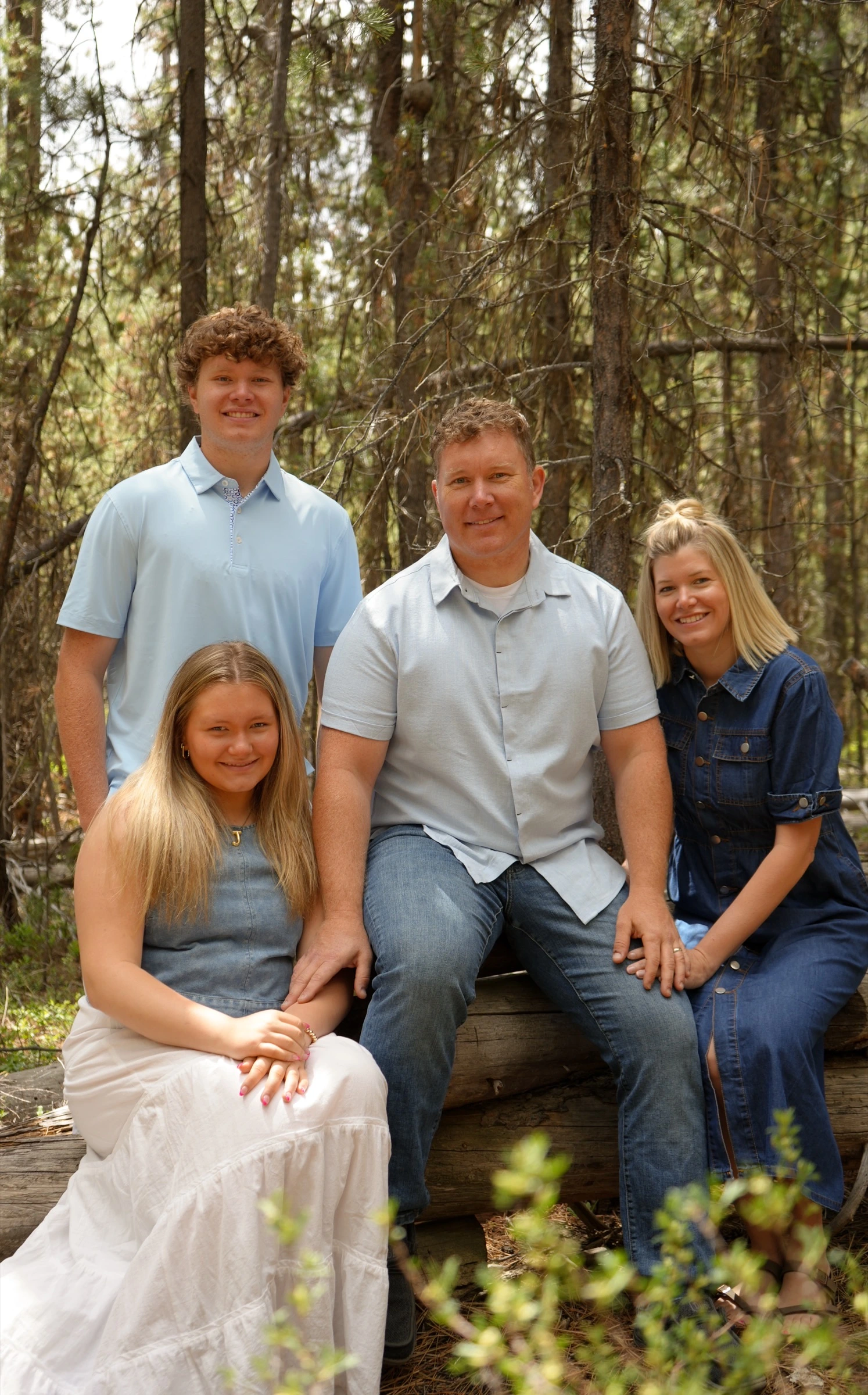 Family of four posed on a fallen log in the forest