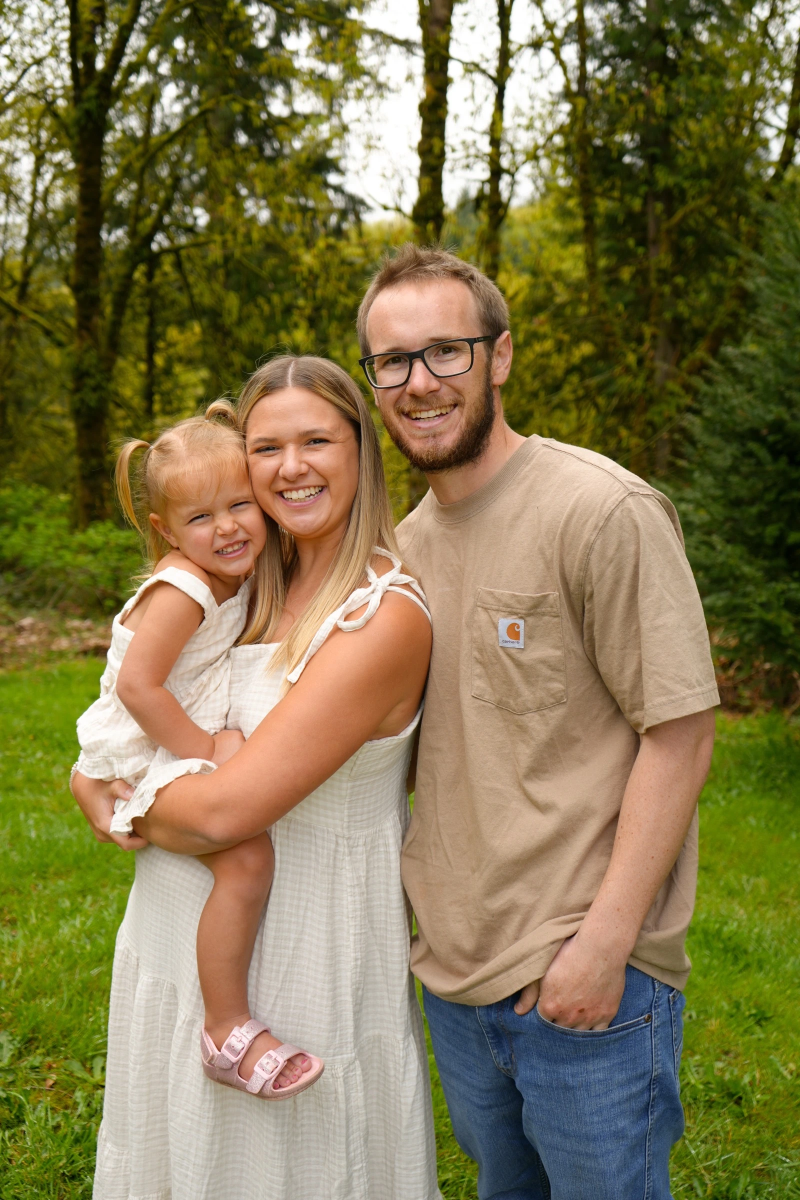Parents with a young child smiling outdoors on a green lawn