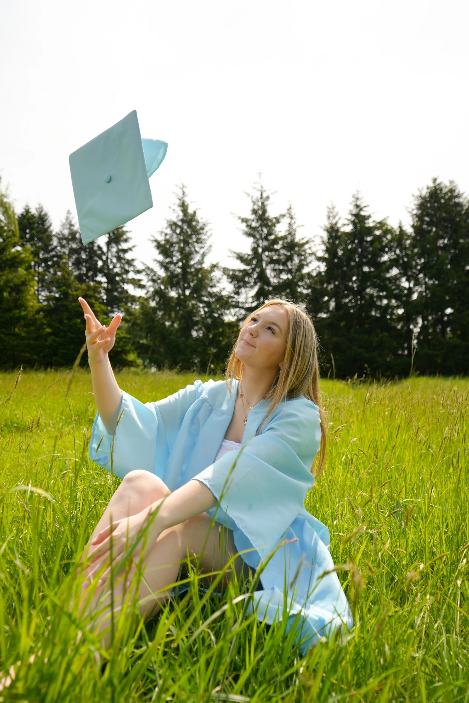 Graduate tossing a light blue cap in a grassy field