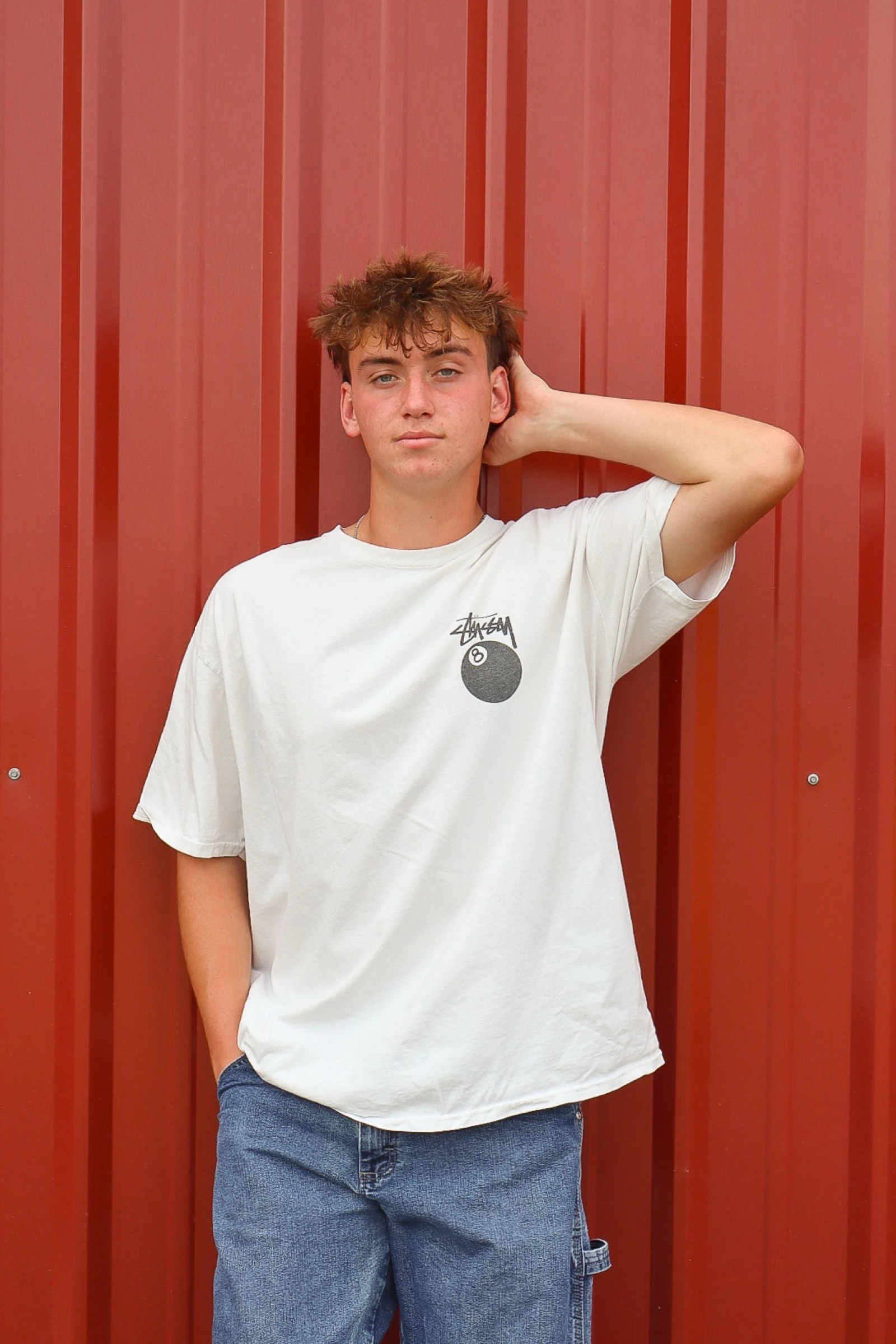Young man in a white tee posing against a corrugated red wall