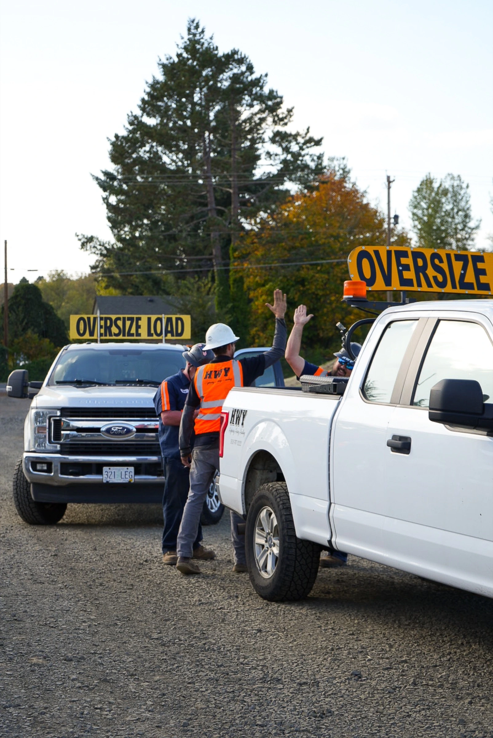 Logistics crew celebrating with a high-five beside white Ford trucks and oversize signs