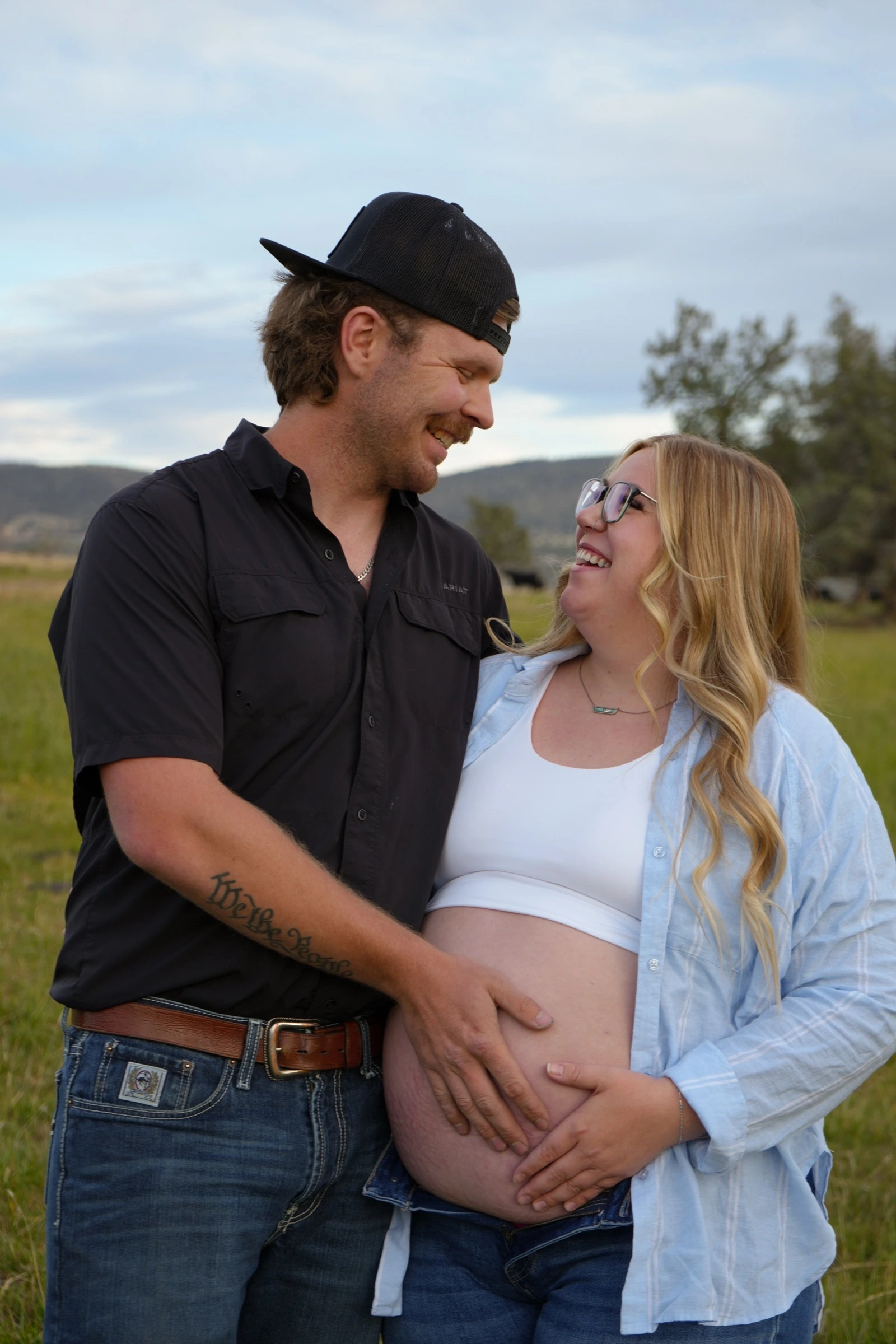 Pregnant couple laughing together outdoors with hands on her belly
