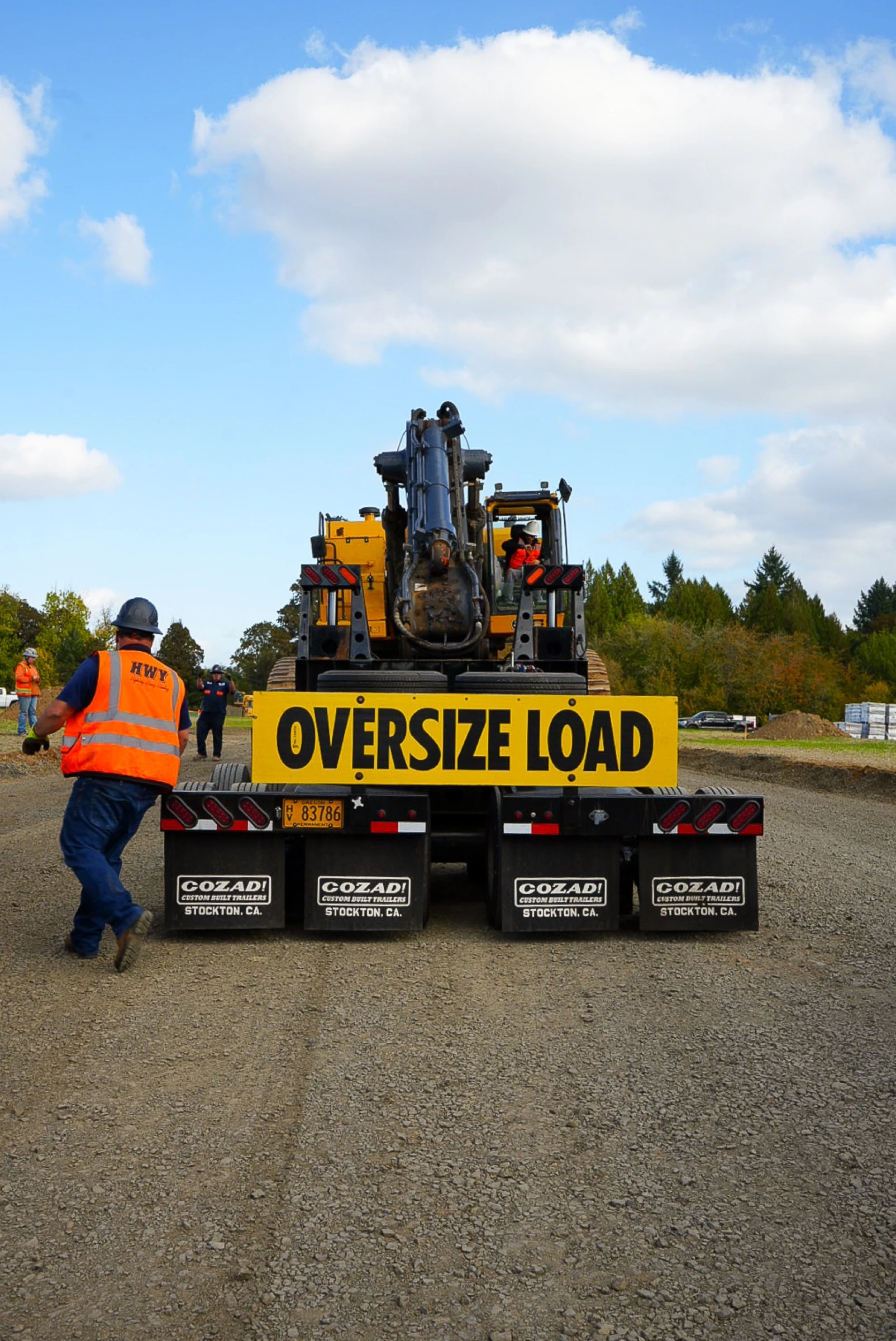 Heavy haul trailer carrying yellow construction equipment with OVERSIZE LOAD signage