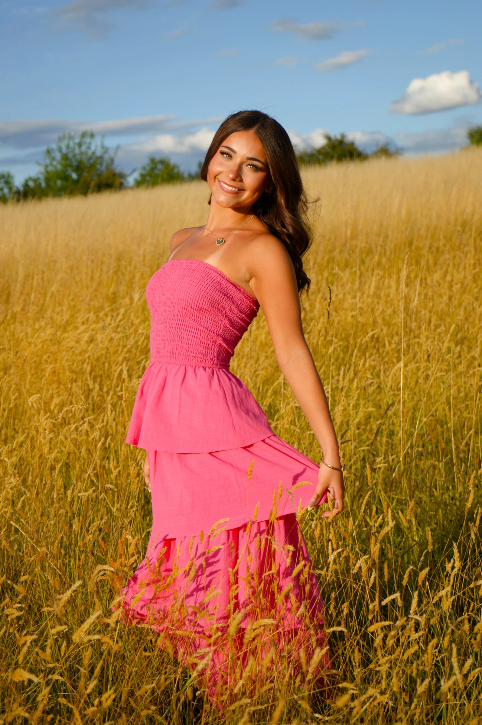 Young woman in a bright pink dress smiling in a golden field at sunset