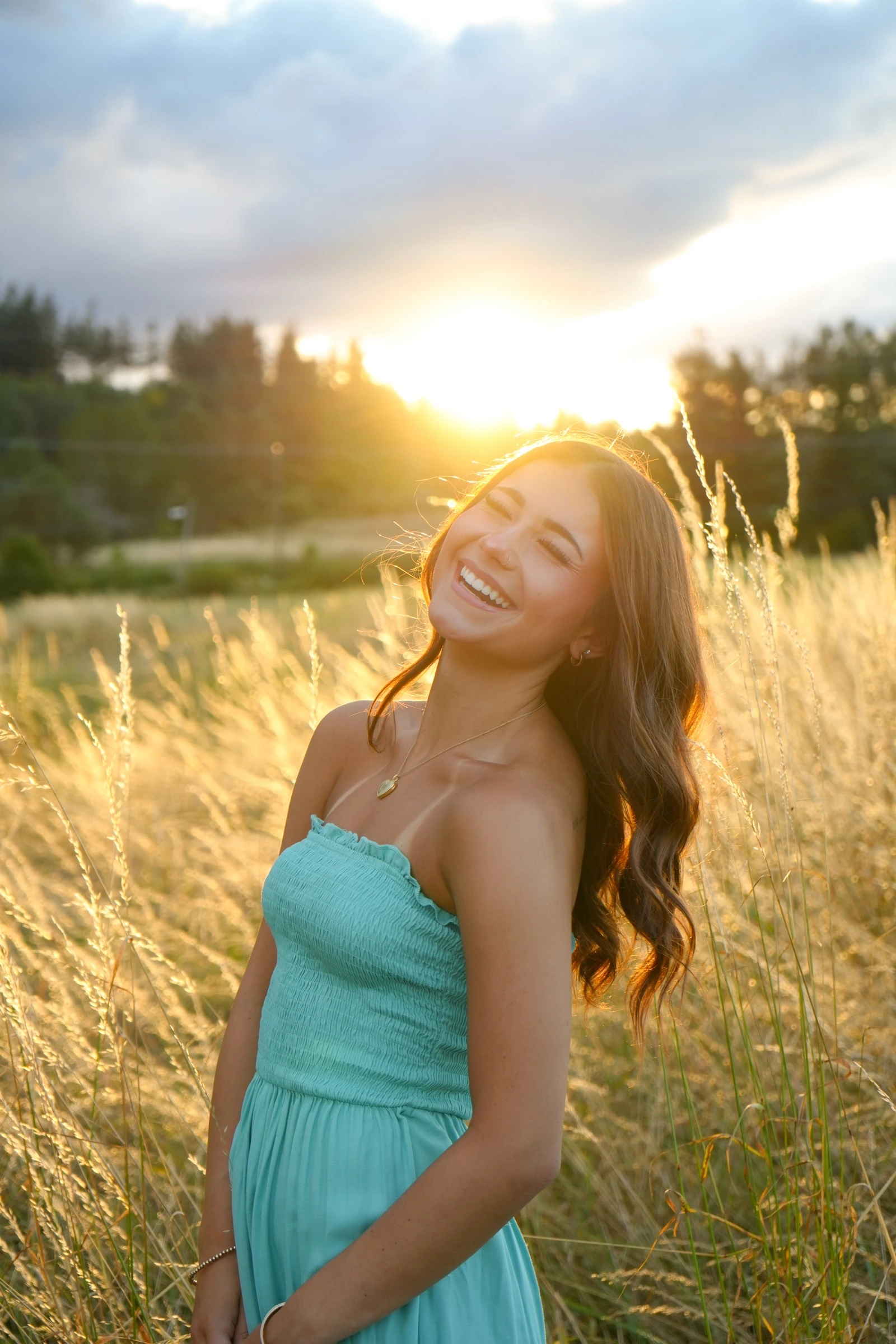 Woman in a teal dress laughing in a sunlit field