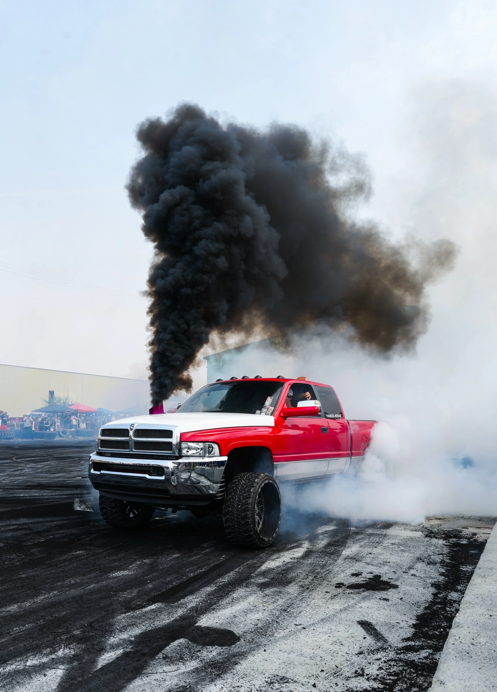 Red and white lifted truck performing a burnout with diesel smoke