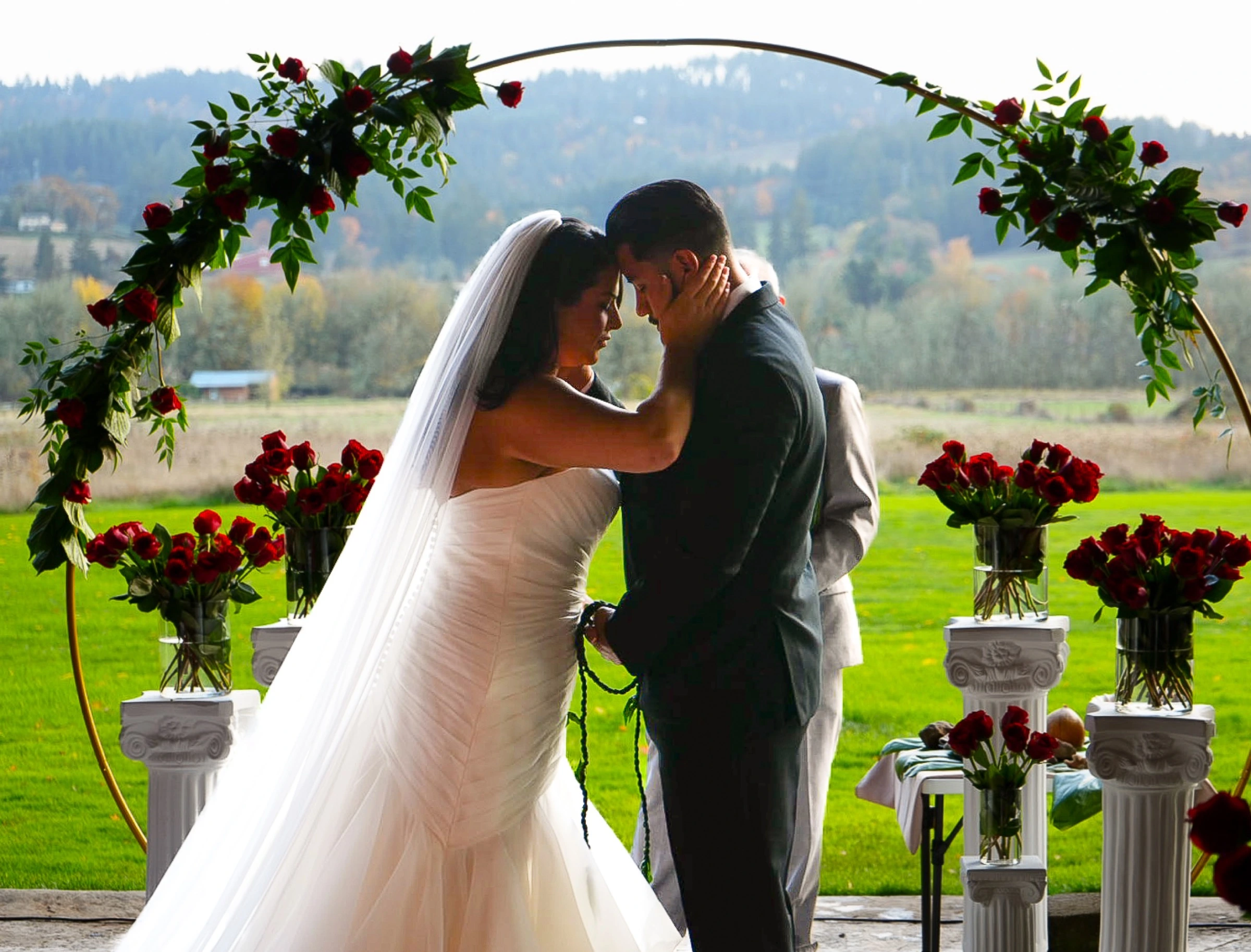 Bride and groom under a floral arch during an outdoor wedding ceremony