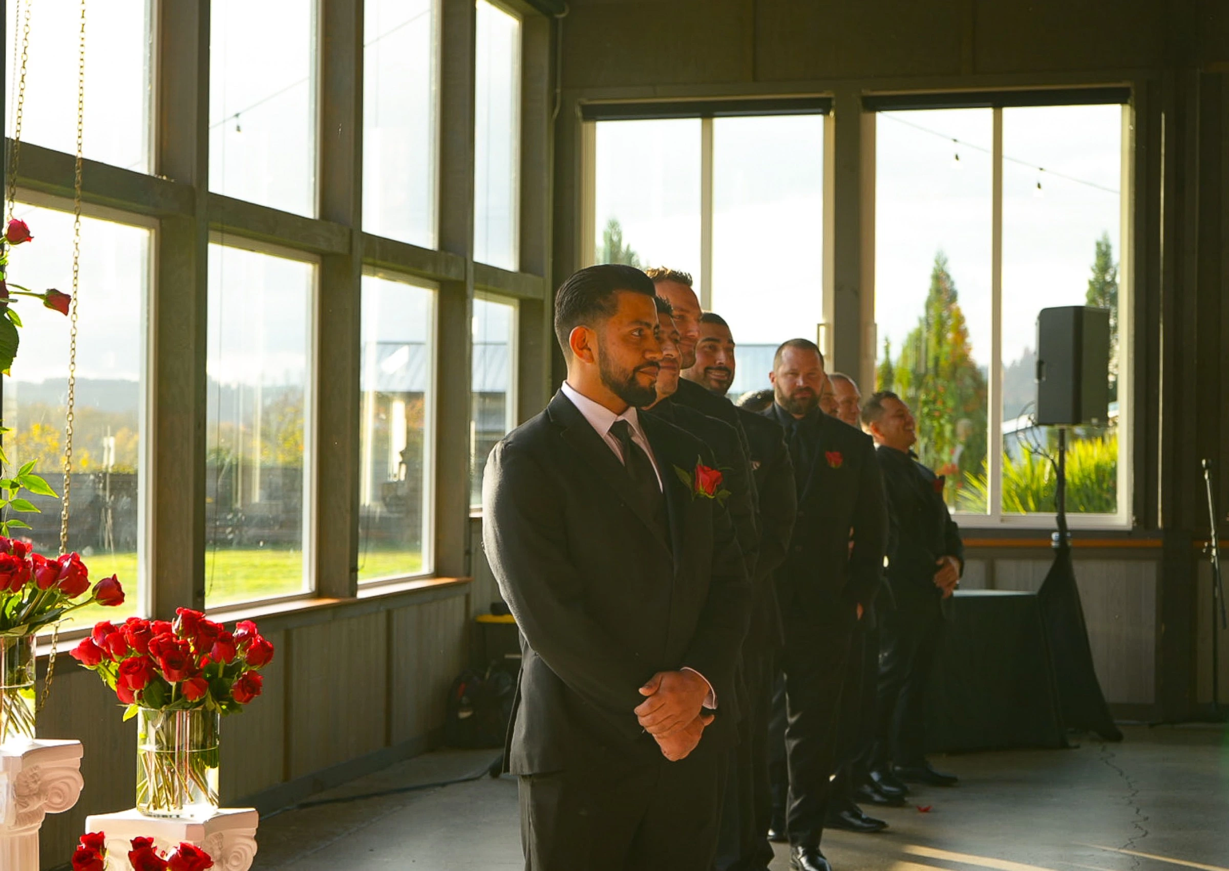 Groom and groomsmen in black suits watching the ceremony indoors